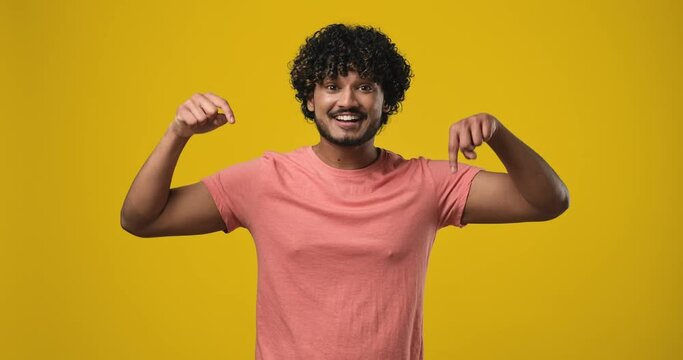 young indian man 20s wear t-shirt point index fingers down on something gesture isolated on orange studio background