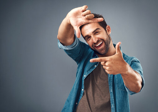 Frame, excited and portrait of man in studio on gray background with happiness, confident and smile. Finger border, face and happy male person with hand sign for picture, photography and perspective