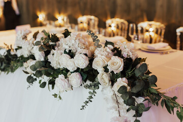 Table for groom and bride decorated with white roses and greenery.	Head table at wedding. 
