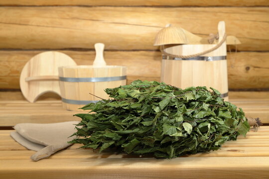 On a wooden bench in the interior of the sauna there is a dry birch broom on the background of traditional wooden bath equipment and accessories.	