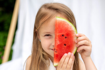 The child is holding a slice of watermelon, covering half of her face with it