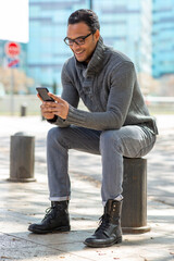 Young african man sitting outside using mobile phone in the city