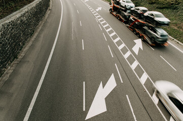 aerial image of a road with an arrow symbol and a truck carrying new cars from the factory , the vehicle is blurred due to movement