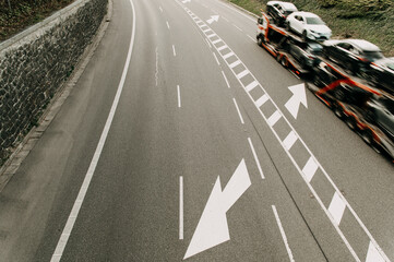 aerial image of a road with an arrow symbol and a truck carrying new cars from the factory , the vehicle is blurred due to movement