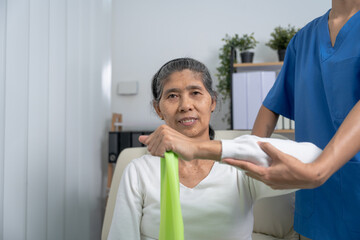 Obraz premium Concept of World Confederation for Physical Therapy. young physiotherapist caregiver helping mature elderly woman training with elastics in rehabilitation center, muscle weakness