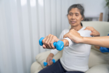 Fototapeta na wymiar Young pretty asian physiotherapist helping senior female patient holding dumbbell in physical therapy session, concept of World Confederation for Physical Therapy.