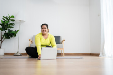 Asian overweight woman doing stretching exercise at home on fitness mat. Home activity training, online fitness class. Stretching training workout on yoga mat at home for good health and body shape.