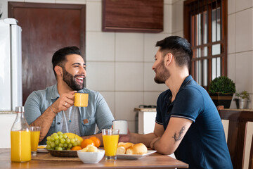brazilian gay couple smiling and talking during breakfast in kitchen table