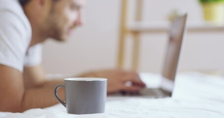 Coffee, bed and a man typing on his laptop in the morning while lying down in his bedroom to relax. Cup, computer and internet blogging with a male browsing social media to wake up in his home