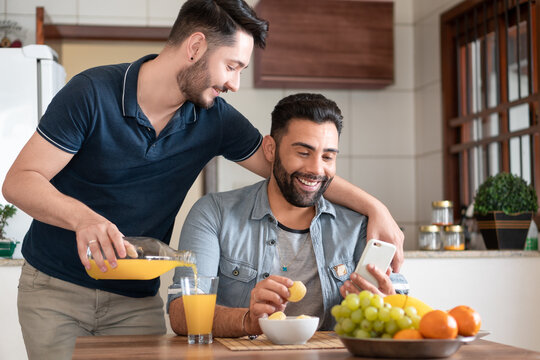 happy gay man serving juice and looking at mobile at table