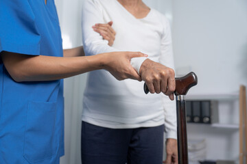 Fototapeta na wymiar Attentive practitioner nurse assisting physical therapy elderly woman on a walking wood standard cane in disability nursing rehabilitation center, physical therapy encourage hands.