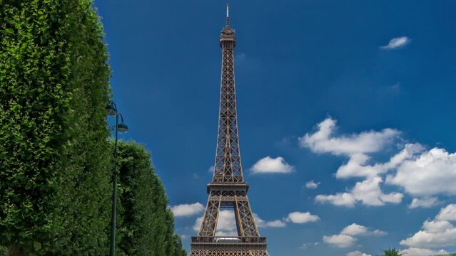 Eiffel Tower on Champs de Mars in Paris timelapse hyperlapse, France. Blue cloudy sky at summer day with green lawn with trees and people walking around.