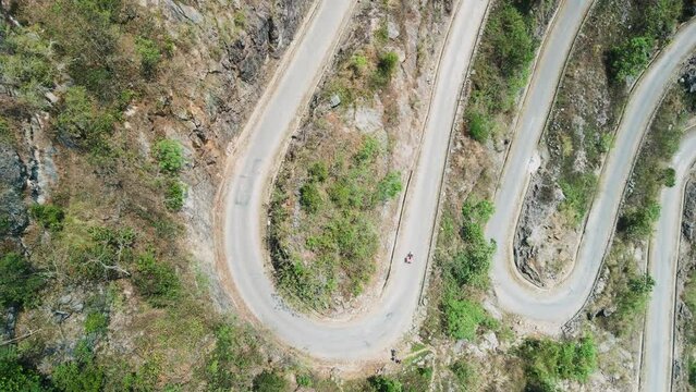 Khau Coc Cha Mountain Pass. Lone vehicle on sharp hair-pin bend. Aerial drone gently rises vertically to reveal series of dramatic, scary bends on steep, twisty mountain road. 