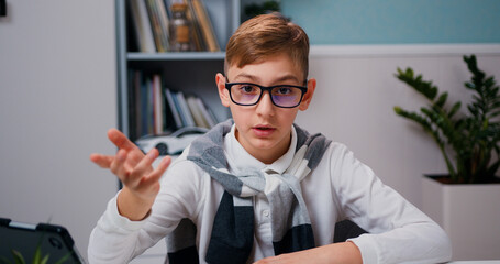 Close up portrait little boy sit on table at home look at camera having peasant lively remote conversation. Caucasian kid having a video chat.