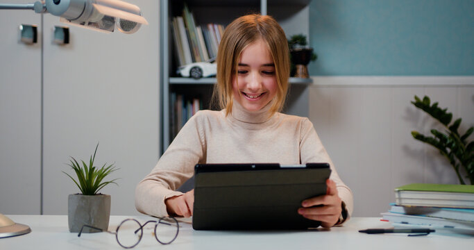 Close up pretty 10s girl sitting in home classroom with tablet device, studying, play video game, use modern wireless tech.