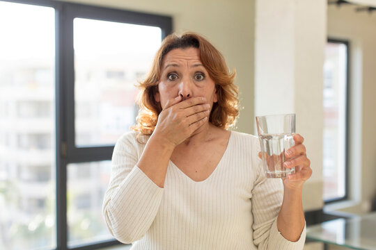 middle age pretty woman covering mouth with a hand and shocked or surprised expression. water glass