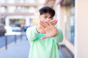 young handsome man covering face with hand and putting other hand up front to stop camera, refusing...
