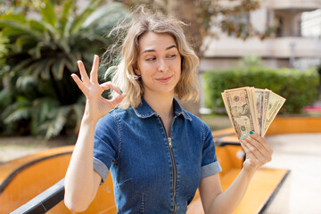 pretty woman feeling happy, showing approval with okay gesture. dollar banknotes concept