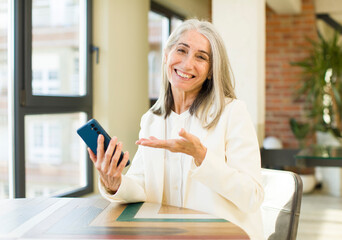 Fototapeta premium pretty senior woman smiling cheerfully, feeling happy and showing a concept with a smartphone
