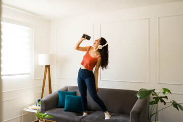 Cheerful woman dancing and singing listening to music with headphones at home