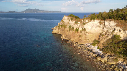Fototapeta premium Rocky cliff of a tropical island. Aerial view of rocky coastline and blue sea at sunset.