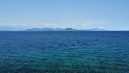 Naklejka na ściany i meble Seascape. Aerial view of the blue sea, white clouds and a tropical island on the horizon.