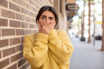 pretty woman covering mouth with hands with a shocked, surprised expression, keeping a secret or...