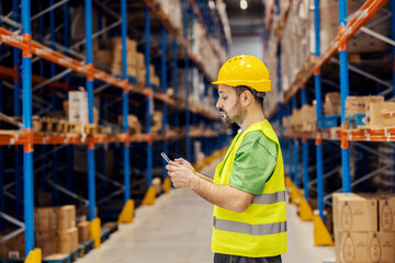 A warehouse clerk is adding orders on tablet while standing in facility.