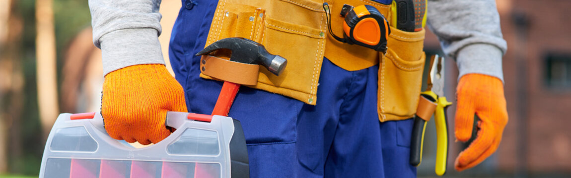 Male builder wearing tool belt carrying toolbox at construction site. Close up on waist area
