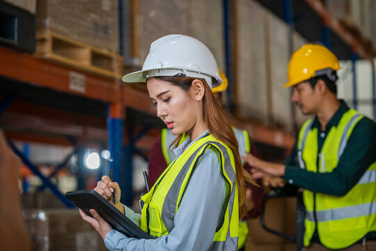 Logistics worker storing package boxes in a large distribution centre,Warehouse worker moving cardboard boxes while working with a colleague in a warehouse,. - Powered by Adobe