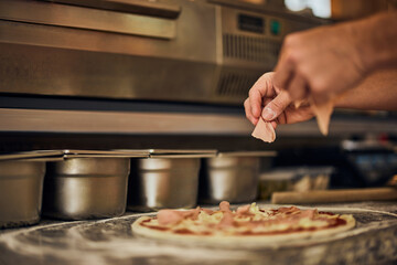 Male hands holding a ham and putting on the pizza dough, making a pizza.