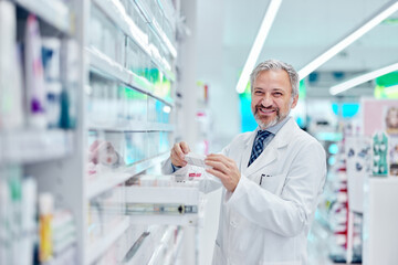 Smiling man working at the pharmacy, posing for the camera while taking something from the drawer.