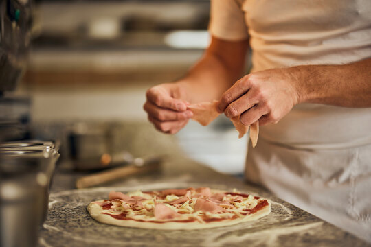 Man holding a ham, putting on a pizza dough, focus on the pizza.