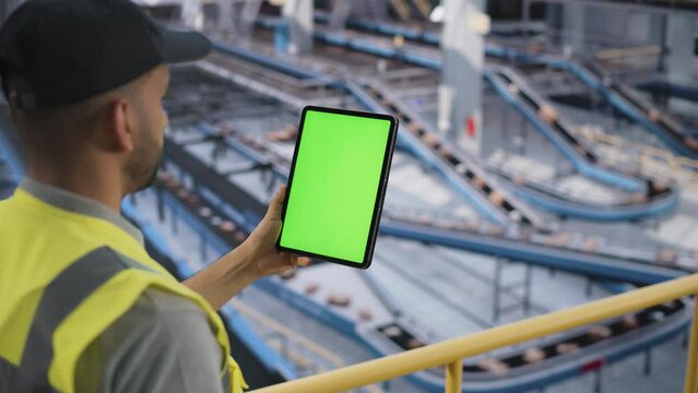 Male Employee Working at a Modern Logistics Center for an International Online Shopping Business. Multiethnic Man Using a Tablet Computer with a Green Screen Mock Up Display