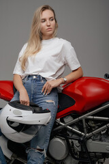 Fototapeta na wymiar Studio shot of blond haired woman motorcyclist around custom motorbike holding helmet.