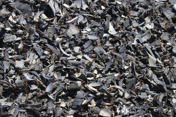 Closeup black background of the bits and pieces of rubber automobile tires heaped on top of each in piles after being shredded by the recycler at the landfill.
