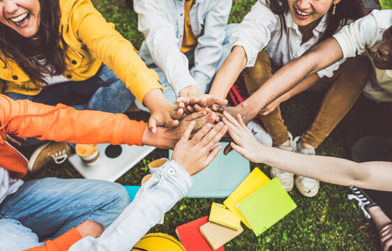Multicultural university students stacking hands together in college campus - Young people hugging outside symbolizing unity and teamwork