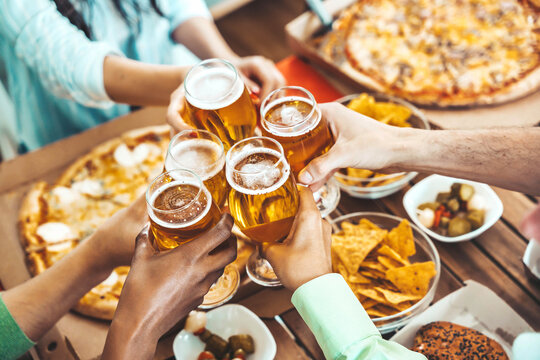 Close-up picture of people drinking beer and eating pizza on balcony at brewery pub table - Happy friends having dinner party at pizzeria restaurant - Dining lifestyle concept 