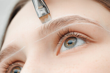 Master draws white guide lines for correction eyebrow of woman in beauty salon