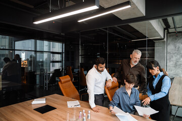 Handsome multiethnic colleagues checking documents behind boss back and talking in office