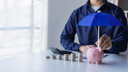 Businessman holding umbrella on pile of money, coins and piggy bank concept Financial insurance and...