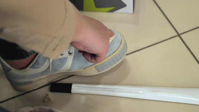 A woman in a shoe shop trying on bright urban trainers. The concept of shopping, fashion and a healthy lifestyle. Close-up of a woman's hands tying laces and checking the tightness with her finger