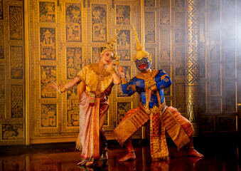 Obraz premium Wide shot of beautiful Asian woman wear Thai traditional dress action of dancing together with Thai classic blue masked and cloths from the Ramakien character with Thai painting on public place wall.