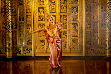 Obraz premium Wide shot of beautiful Asian woman wear Thai ancient traditional dress action of dancing in front of Thai painting as background in public place.