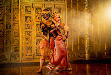 Fototapeta premium Close up beautiful Asian woman wear Thai traditional dress action of dancing together with Thai classic masked from the Ramakien character as black monkey with Thai painting on public place wall.