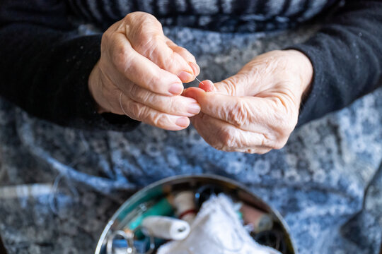 Close-up, hands of a senior woman threading a needle with thread