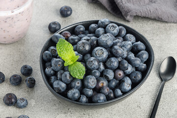 Natural blueberries in a black bowl with mint on gray background, close up