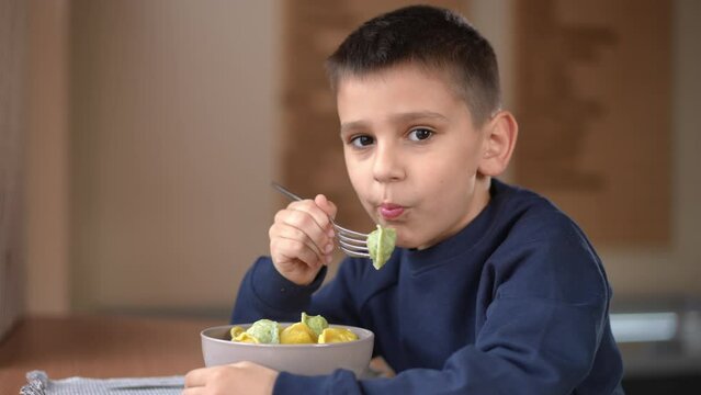 Happy boy eating dumpling in slow motion looking at camera gesturing thumb up. Portrait of confident relaxed Caucasian kid posing dining in cafe indoors
