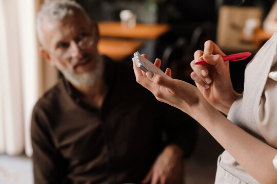 Close-up view of waitress writes down order of elderly man in cafe - Powered by Adobe
