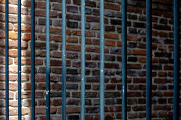 Fototapeta na wymiar Prison cell or jail concept, Selective focus of iron cage with brick block wall backdrop, Old vintage steel gate for convicts, Abstract pattern background.